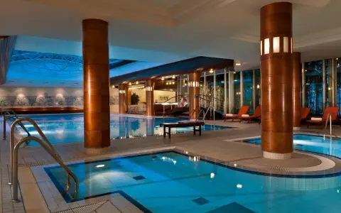 Basen hotelowy Radisson Blu Radebeul z niebieską wodą, drewnianymi kolumnami i leżakami.