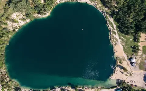 Serce polskiego balatonu, turkusowa woda, otoczona zielenią i piaszczystymi plażami. W oddali widać małą łódkę.
