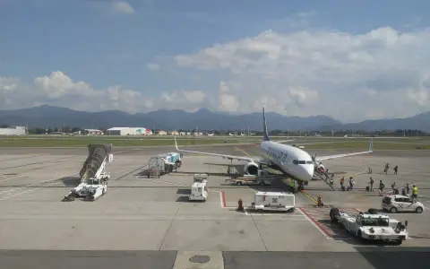 Samolot Ryanair na płycie lotniska Bergamo. W tle góry, na pierwszym planie schody, pojazdy obsługi naziemnej i pasażerowie.