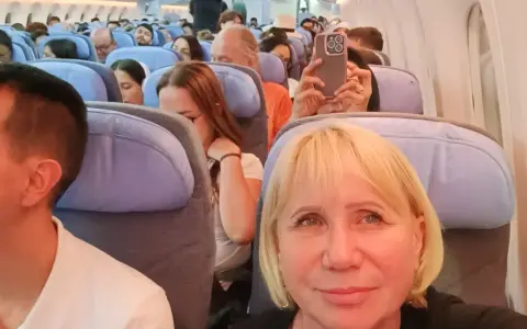 W samolocie, przygotowując się na najdłuższy lot samolotem, pasażerowie siedzą w rzędach. Kobieta robi zdjęcie telefonem.