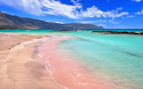 Różowa plaża Elafonisi z turkusową wodą i górami w tle. Idealne miejsce na relaks.
