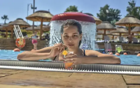 Kobieta w basenie z drinkiem, relaksująca się w słońcu. Idealny dzień all inclusive soft.