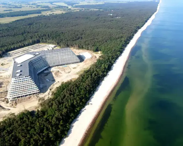 Nowy hotel Gołębiewski w budowie, majestatycznie wznoszący się nad piaszczystą plażą i lasem sosnowym, tuż przy turkusowym morzu.