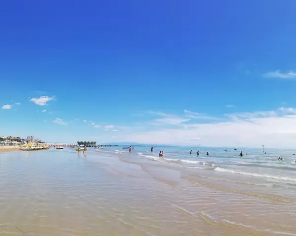 Słoneczna triest plaża piaszczysta z turkusową wodą i błękitnym niebem. Ludzie kąpią się i relaksują.