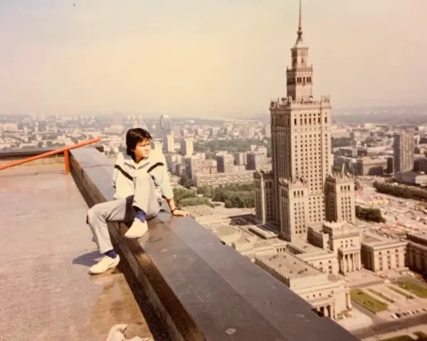 Młody mężczyzna siedzi na dachu, patrząc na panoramę Warszawy. W tle Pałac Kultury i Nauki, który wtedy był najwyższym budynkiem, zanim powstał Marriott.