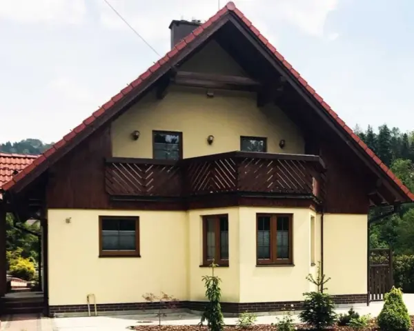 Jasny dom z drewnianymi elementami i balkonem, otoczony zielenią. Może to być dom Adama Małysza w Wiśle.