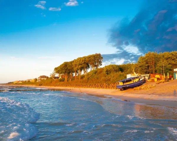 Zachód słońca nad morzem, idealny na zwiedzanie Ustronia i okolic. Piękna plaża, falochrony i łódź na piasku.