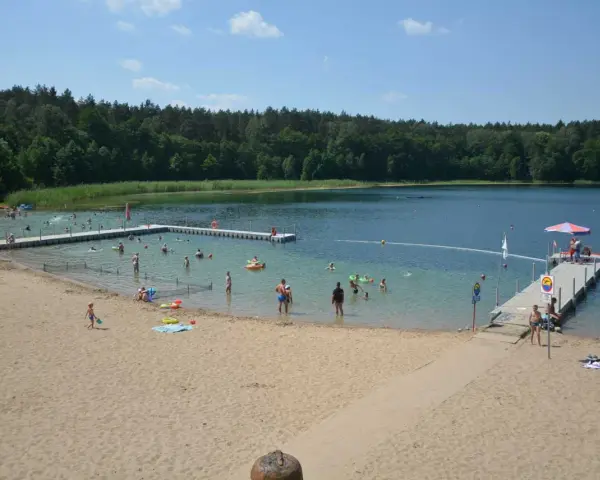 Słoneczny dzień nad jeziorem płotki. Ludzie kąpią się, pływają na dmuchanych zabawkach i odpoczywają na piaszczystej plaży.