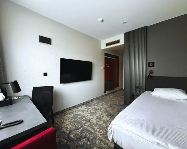 Pokój w hotelu Qubus Gorzów: łóżko, biurko, TV i drzwi do łazienki.