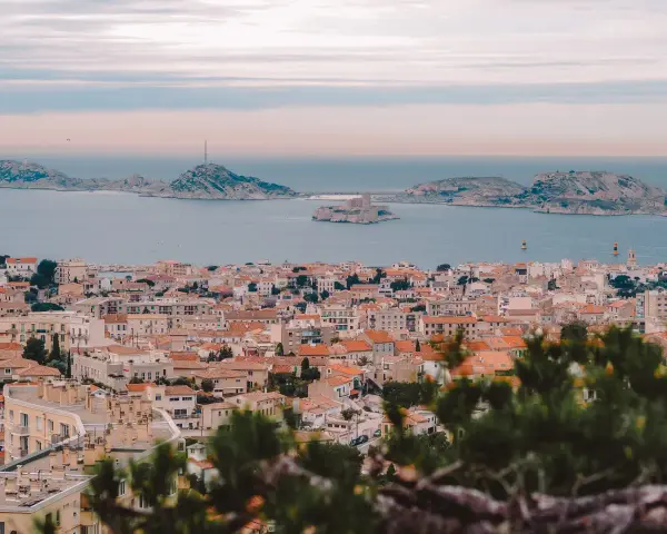 Widok na miasto z dachami i morzem w tle, z widocznym zamkiem na wyspie. To piękne **Marseille**.