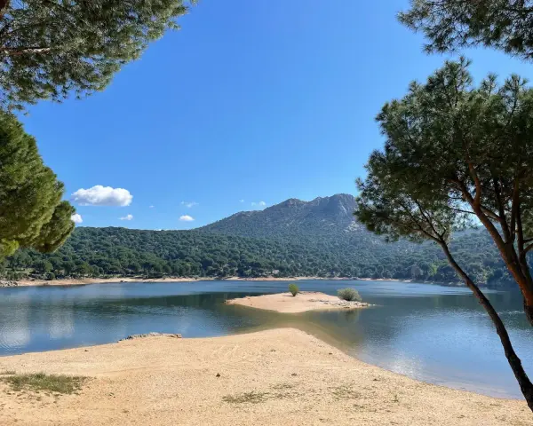 Piękna, piaszczysta plaża nad jeziorem w pobliżu Madrytu, otoczona sosnowym lasem i górami.