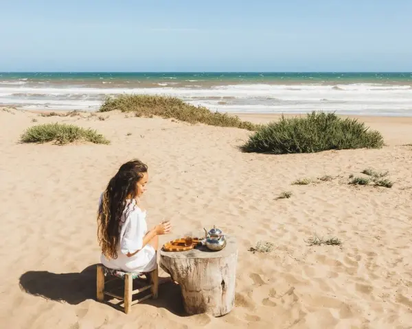 Kobieta pije herbatę na piaszczystych plażach Tunezji, z widokiem na ocean.