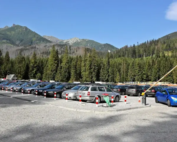 Parking przy wejściu na Morskie Oko. Rząd samochodów pod górskimi szczytami i gęstym lasem.