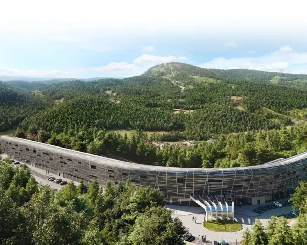 Nowy hotel w górach, o futurystycznym, zakrzywionym kształcie, otoczony gęstym lasem iglastym. W tle widać łagodne, zalesione wzgórza.
