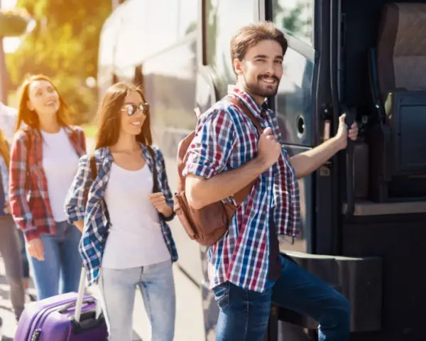 Grupa młodych ludzi z plecakami i walizką wsiada do autobusu, gotowa na wycieczki fakultatywne.
