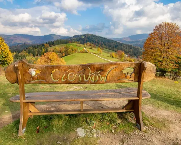 Drewniana ławka z napisem "Ciechocinek" na tle jesiennych gór i zielonych wzgórz. Widok na Beskid Sądecki.