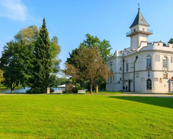 Biały pałac z wieżą, otoczony zielenią, nad jeziorem. Jeden z urokliwych zamków na Mazowszu.