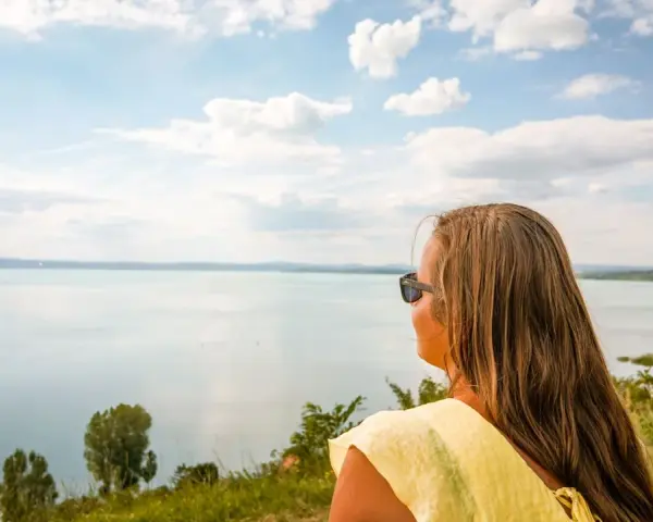 Kobieta w żółtej bluzce podziwia rozległe jezioro Balaton.
