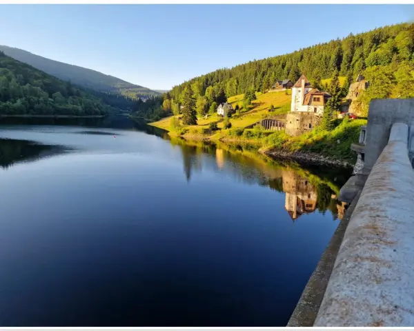Spokojna tafla jeziora odbija zamek i zalesione wzgórza czeskich Karkonoszy.