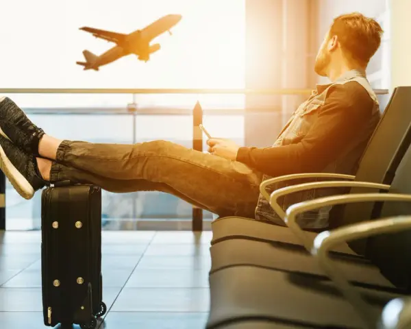 Mężczyzna z nogami na walizce czeka na lotnisku. Samolot startuje. Czyżby czekał na niego, czy to tylko efekt **overbooking**?