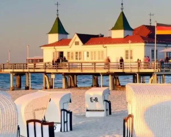 Plaża z koszami i molo, gdzie widać budynek restauracji i niemiecką flagę. Atrakcje po niemieckiej stronie Świnoujścia zachęcają do spacerów.