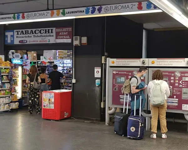 Przystanek autobusowy w Rzymie Ciampino. Ludzie kupują bilety i artykuły w sklepie.