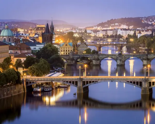 Praga nocą, z wieloma mostami na Wełtawie i oświetlonymi budynkami. Ciekawe ciekawostki o Czechach czekają na odkrycie w tym magicznym mieście.