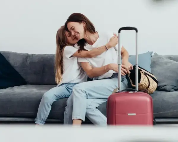 Mama i córka przytulają się na kanapie, obok walizka. Wszyscy, którzy chcą zameldować się w hotelu, mogą tu poczuć się jak w domu.