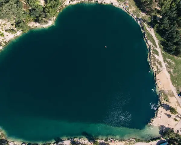 Serce polskiego balatonu, turkusowa woda, otoczona zielenią i piaszczystymi plażami. W oddali widać małą łódkę.