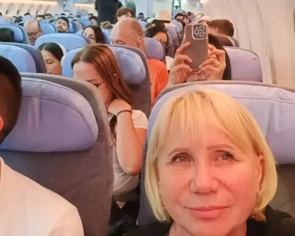 W samolocie, przygotowując się na najdłuższy lot samolotem, pasażerowie siedzą w rzędach. Kobieta robi zdjęcie telefonem.