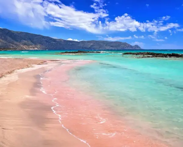 Różowa plaża Elafonisi z turkusową wodą i górami w tle. Idealne miejsce na relaks.