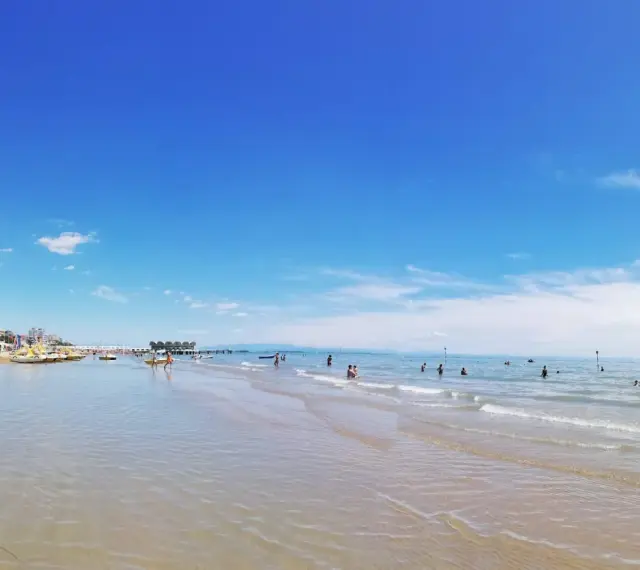 Słoneczna triest plaża piaszczysta z turkusową wodą i błękitnym niebem. Ludzie kąpią się i relaksują.