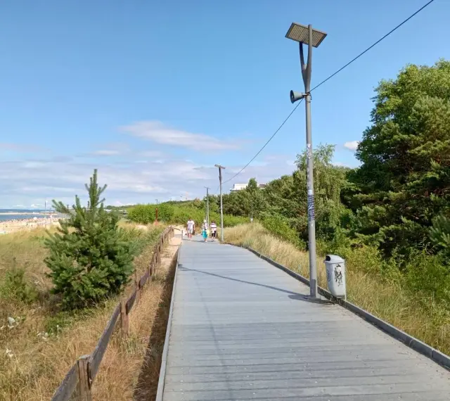 Spacer po promenadzie w Świnoujściu. Widok na plażę, morze i zielone drzewa. Atrakcje dla spacerowiczów.