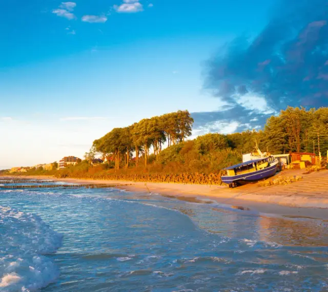 Zachód słońca nad morzem, idealny na zwiedzanie Ustronia i okolic. Piękna plaża, falochrony i łódź na piasku.