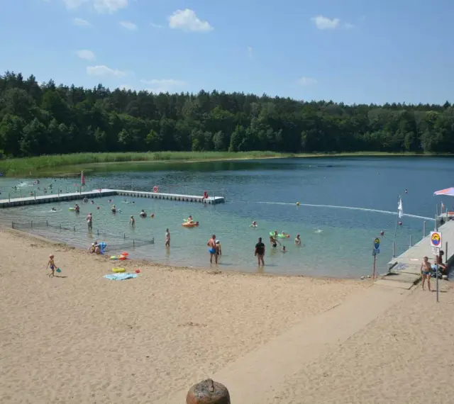 Słoneczny dzień nad jeziorem płotki. Ludzie kąpią się, pływają na dmuchanych zabawkach i odpoczywają na piaszczystej plaży.