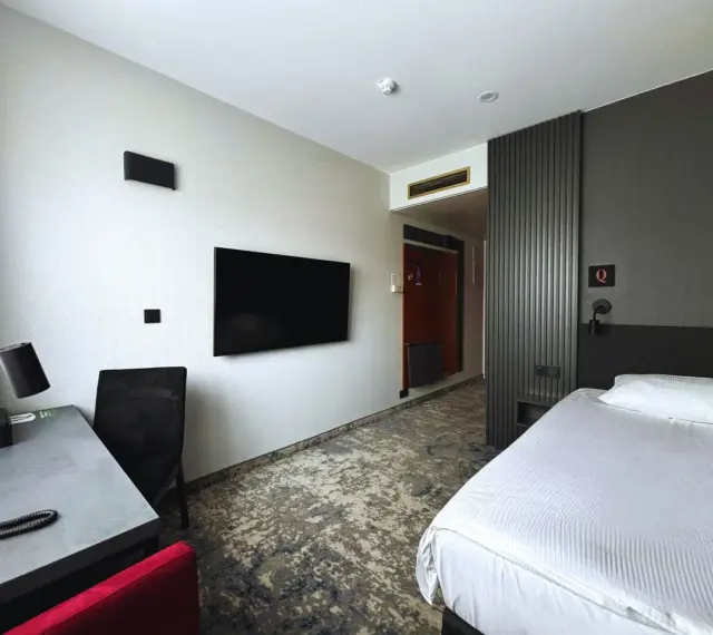Pokój w hotelu Qubus Gorzów: łóżko, biurko, TV i drzwi do łazienki.