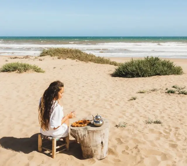 Kobieta pije herbatę na piaszczystych plażach Tunezji, z widokiem na ocean.