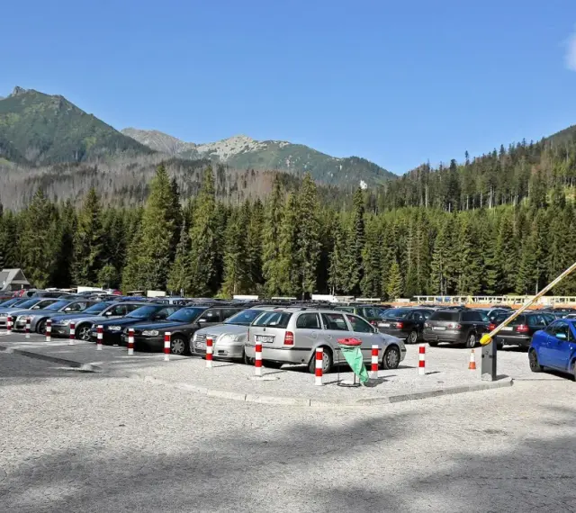 Parking przy wejściu na Morskie Oko. Rząd samochodów pod górskimi szczytami i gęstym lasem.