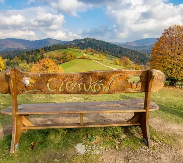 Drewniana ławka z napisem "Ciechocinek" na tle jesiennych gór i zielonych wzgórz. Widok na Beskid Sądecki.