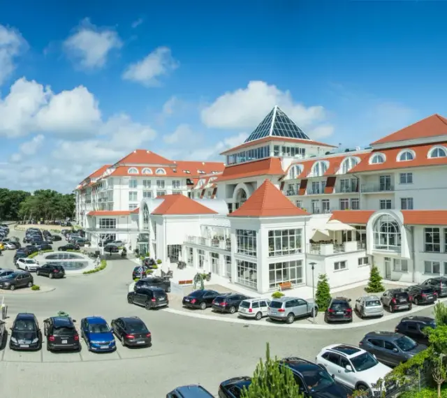 Elegancki hotel 5 gwiazdkowy nad morzem z przestronnym parkingiem pełnym samochodów.