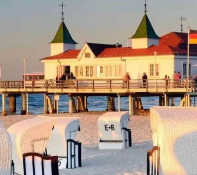 Plaża z koszami i molo, gdzie widać budynek restauracji i niemiecką flagę. Atrakcje po niemieckiej stronie Świnoujścia zachęcają do spacerów.