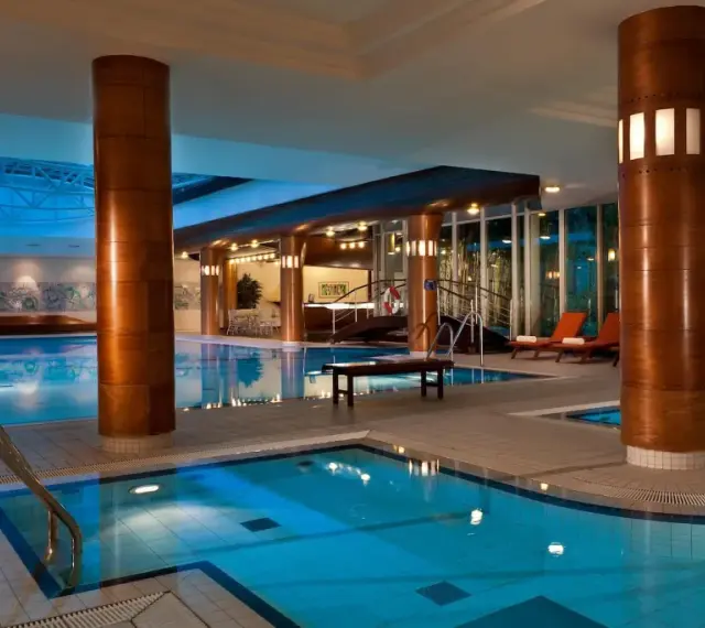 Basen hotelowy Radisson Blu Radebeul z niebieską wodą, drewnianymi kolumnami i leżakami.