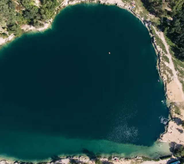Serce polskiego balatonu, turkusowa woda, otoczona zielenią i piaszczystymi plażami. W oddali widać małą łódkę.
