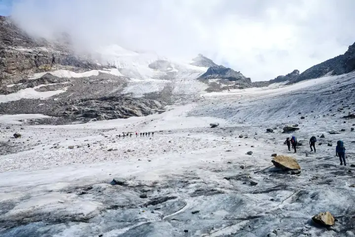 Grupa turystów wędruje po lodowcu w kierunku majestatycznego masywu Monte Rosa.