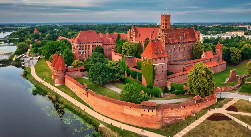 Malbork, największy zamek w Polsce, majestatycznie wznosi się nad rzeką Nogat. Czerwona cegła i strzeliste wieże tworzą imponujący widok.