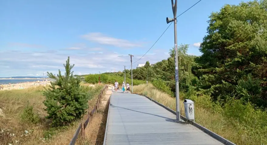 Spacer po promenadzie w Świnoujściu. Widok na plażę, morze i zielone drzewa. Atrakcje dla spacerowiczów.