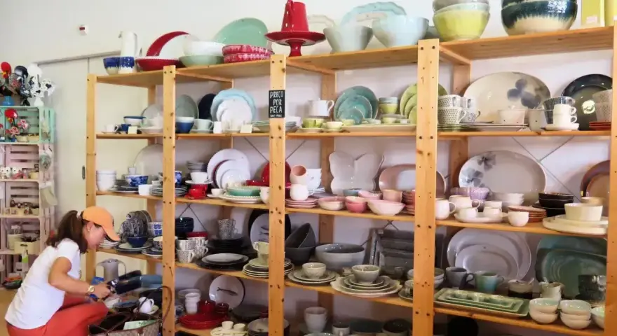 Kobieta wybiera ceramiczne naczynia, idealne pamiątki, które warto co przywieźć z Portugalii. Kolorowe talerze, miski i filiżanki na drewnianych półkach.