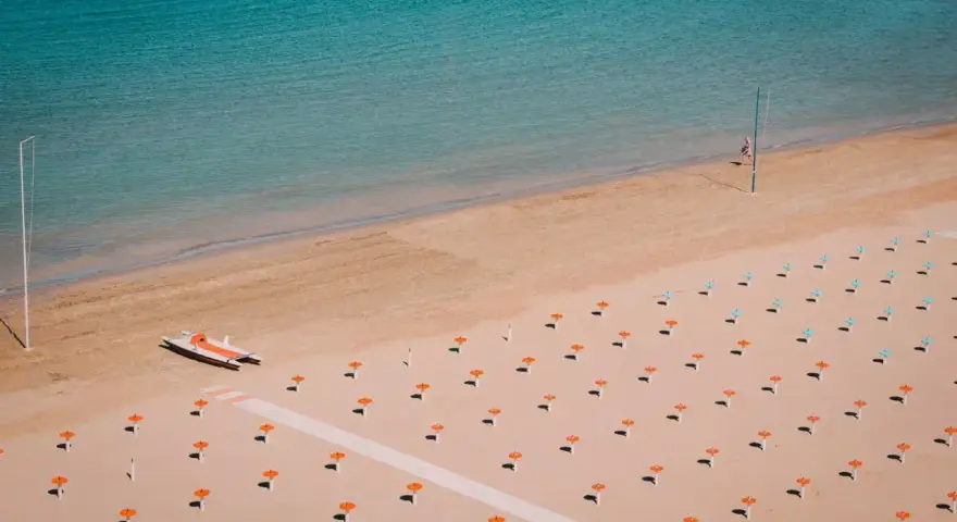 Pusta plaża w Rimini z rzędami pomarańczowych parasoli i łodzią ratowniczą.