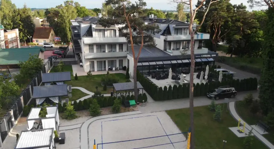 Nowoczesny hotel Cristal Spa z basenem i kortem do siatkówki plażowej, otoczony zielenią.