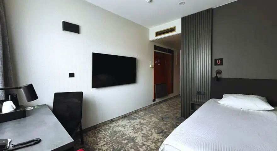 Pokój w hotelu Qubus Gorzów: łóżko, biurko, TV i drzwi do łazienki.